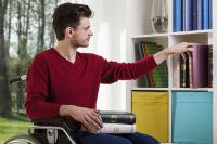 Un homme en fauteuil roulant choisit des livres dans une bibliothèque