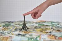 Une main touche une Tour Eiffel placée sur de nombreux billets