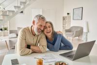 Un couple regarde un ordinateur portable en riant. Les deux seniors sont dans intérieur épuré.