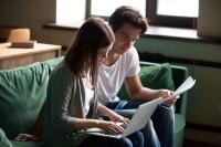 Jeune couple assis sur un canapé examinant des comptes ou factures avec un ordinateur portable.