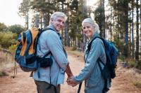 Portrait d’un couple âgé se retournant en souriant et se tenant la main en promenade dans une forêt.