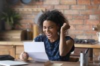 Une femme sourit et lève le bras à la lecture d’un contrat