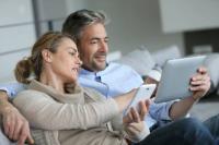 Un couple compare des documents devant une tablette et un smartphone.