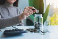 Une femme met des pièces de monnaie dans un bocal en verre 