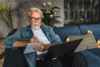 Homme sur un canapé prenant des notes devant un ordinateur portable