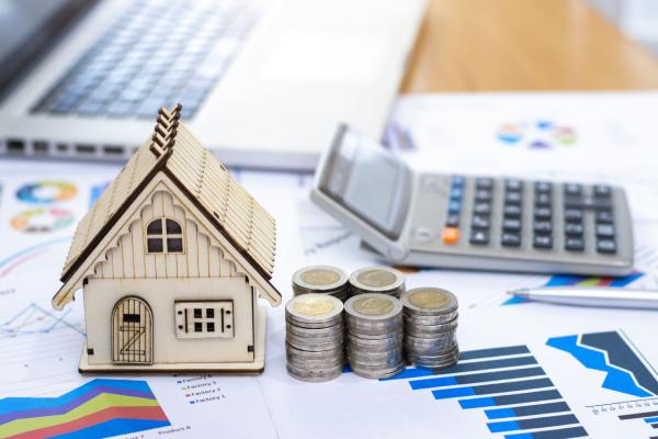 Une maquette d’une maison est posée à proximité d’une pile de pièces et d’une calculatrice.