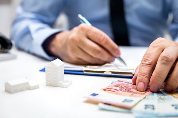 Un homme tient un stylo à côté de billets d’euros.