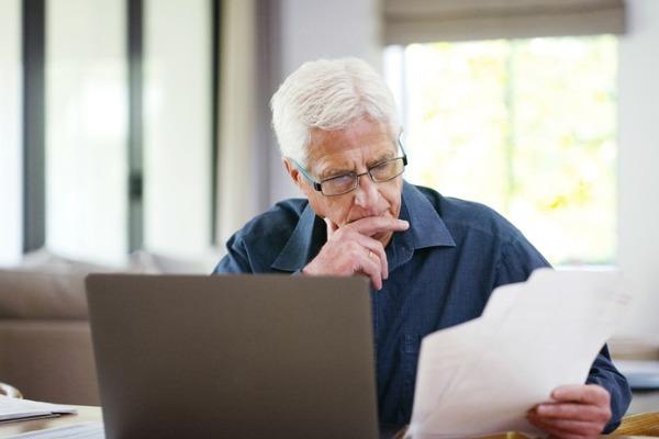 Un homme aux cheveux blancs lit des documents devant son ordinateur 