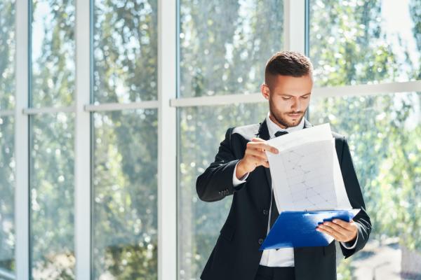 Un homme debout devant une fenêtre lit un contrat