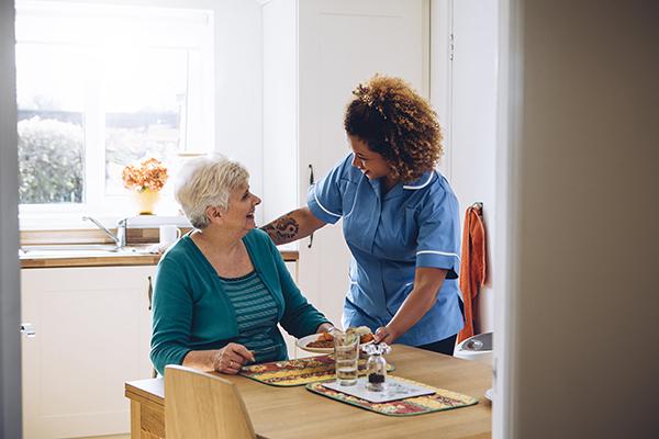 Une femme aide une personne âgée à prendre son repas. 