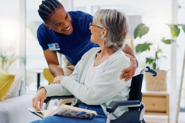 Femme en fauteuil roulant accompagnée par un aide soignant souriant en blouse bleue. 