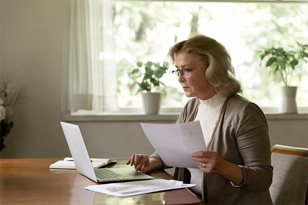 Une femme d'âge mure consulte des documents et son ordinateur portable