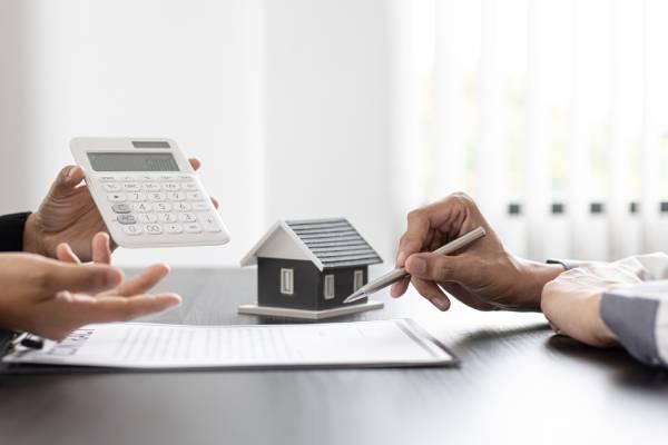 Deux personnes discutent à côté d’une maquette de maison. L’une tient une calculatrice, l’autre un stylo.