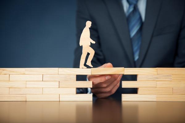 Un personnage marche sur une passerelle en bois soutenue par une main