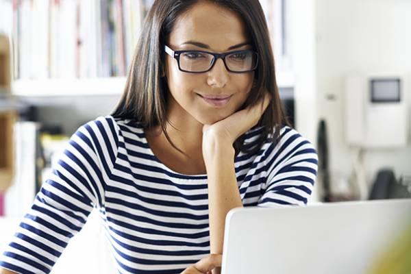 Une jeune femme regarde un écran d’ordinateur en souriant