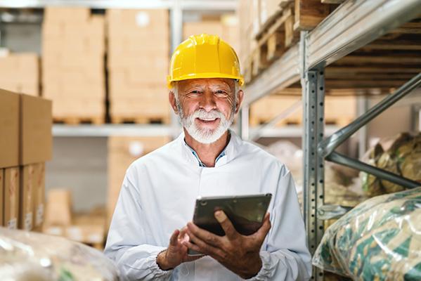 Un senior portant un casque de chantier et tenant une tablette dans un entrepôt