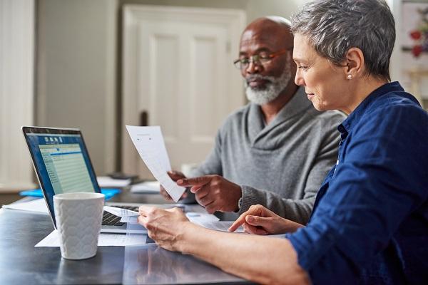 Un couple âgé étudie attentivement leur budget d’assurance sur un ordinateur et des documents papiers